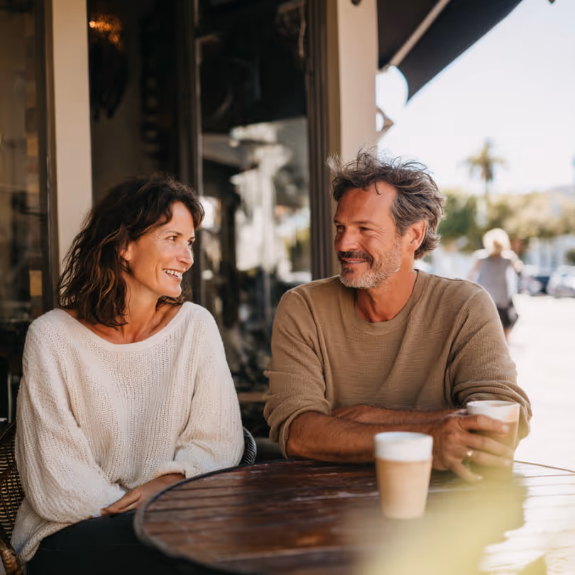 Smiling couple sitting at an outdoor café table, each holding a coffee cup.